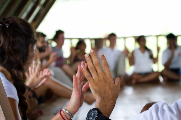 A circle of individuals with focal point on two hands connecting.
